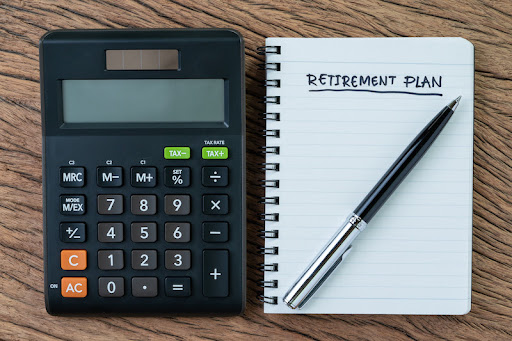 Retirement planning concept, calculator with empty notepad with pen and handwriting underline headline as Retirement Plan on wood table, plan of saving and investment for expense after retire life.