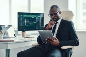 Concentrated young African man in formalwear using modern technologies while working in the office